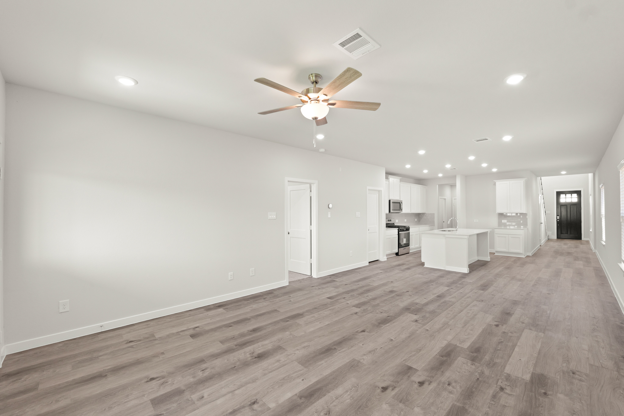A large empty room with a ceiling fan and a wood floor.
